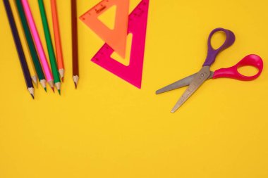 Sarı arka planda makas, cetvel ve renkli kalemler. kırtasiye ögeleri