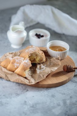 Lezzetli kahvaltı konsepti, yakın plan. Kremalı kırık bir kruvasan tahtanın üzerinde, bal kasesi ve bir sürahi kremayla birlikte duruyor..