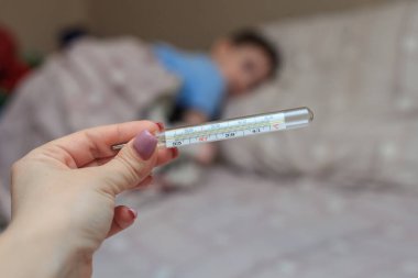 Cıva termometresi, ellerinde sıcaklık olan yakın plan, bir çocukla bulanık bir arkaplan. Coronovirus. Hastalık