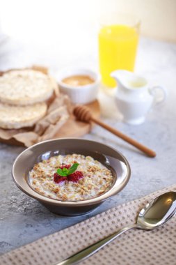 Sağlıklı ve besleyici bir kahvaltı. Bir tabakta süt ve ahududu, tam tahıllı ekmek ve taze sıkılmış meyve suyu ile pişirilmiş granola. Nefis müsli..