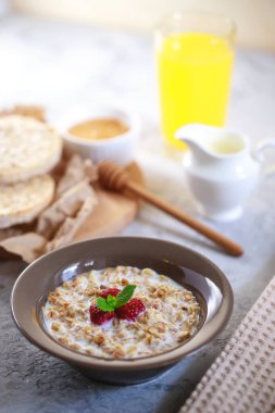 Sağlıklı ve besleyici bir kahvaltı. Bir tabakta süt ve ahududu, tam tahıllı ekmek ve taze sıkılmış meyve suyu ile pişirilmiş granola. Nefis müsli..