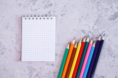 Gri arka planda, renkli kalemlerle dolu beyaz boş bir sayfa. Mesaj için alan, arkaplan. Ofis, kırtasiye