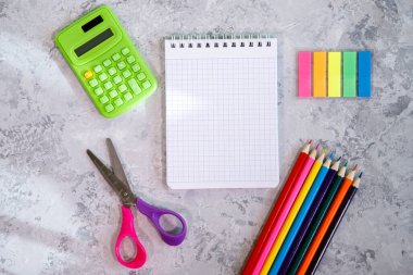 Kırtasiye seti, hesap makinesi, not defteri, renkli kalemler, renkli çıkartmalar, gri arkaplanda makas. Mesaj için alan, arkaplan. Düz yatış, üst görünüm