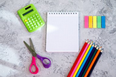 Kırtasiye seti, hesap makinesi, not defteri, renkli kalemler, renkli çıkartmalar, gri arkaplanda makas. Mesaj için alan, arkaplan. Düz yatış, üst görünüm