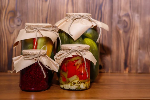 Jar of raspberry jam with canned jars of vegetables on a wooden background. Preserves.