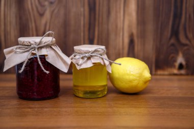 Soğuk algınlığı ve grip için önlem. Ahşap zemin üzerinde ahududu reçeli, bal ve limon, metin için yer.