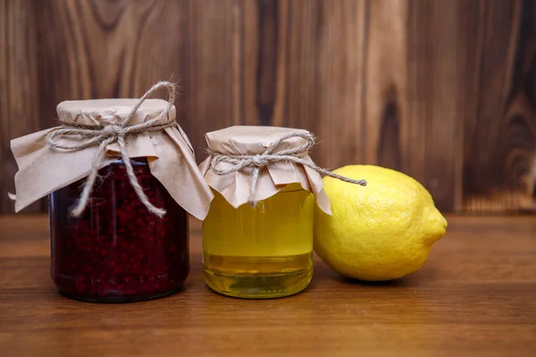Prevention for colds, flu. Raspberry jam, honey and lemon on a wooden background, space for text.