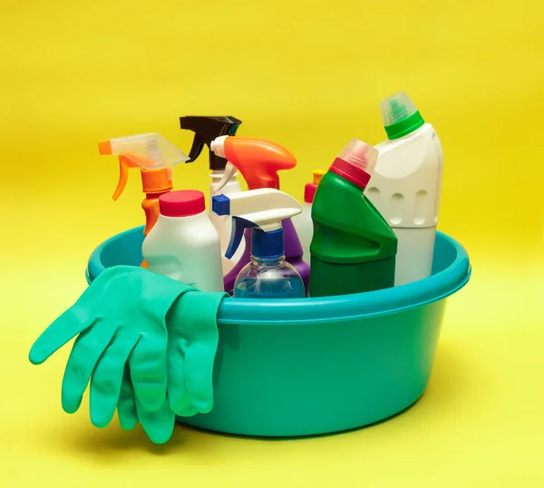 Cleaning. Bottles with cleaning products and detergents in a blue basin on a yellow background. Cleaning, disinfection. Sanitation. Space for text.