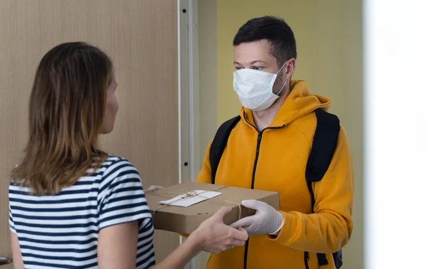 Man from delivery service in medical mask handing pizza to a woman