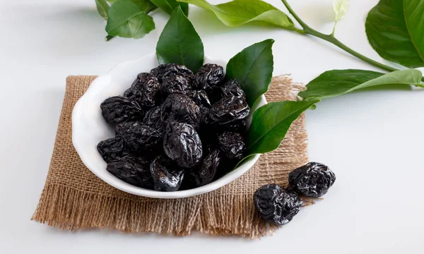 Bowl of sweet dried plums with lemon leaves on a white backgroun — Stock Photo, Image