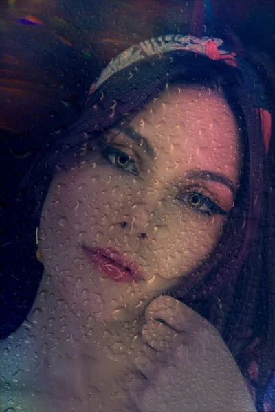 Face of beautiful romantic girl through a window glass with rain — Stock Photo, Image