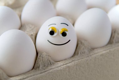 Karton kutuda yumurtalar, komik boyalı gülen yüzlü bir yumurta.