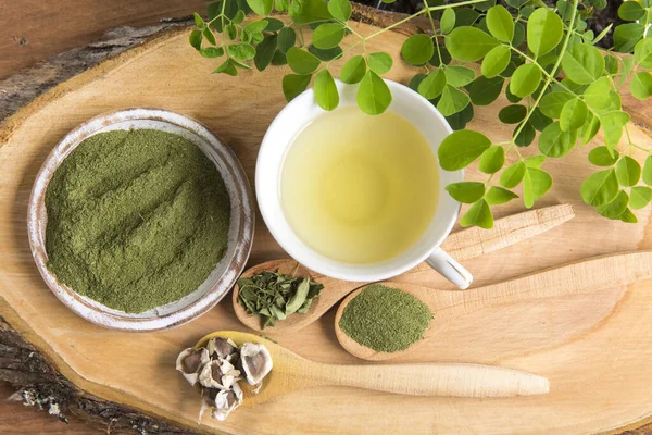 Moringa çayı, yapraklar, tohumlar, tahta bir arka planda toz - Moringa oleifera