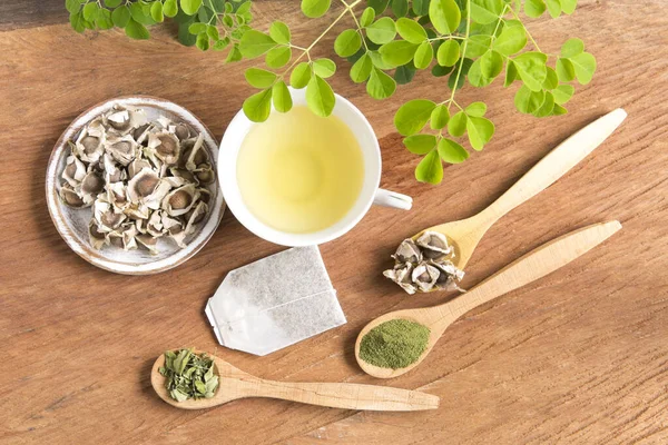 Moringa çayı, yapraklar, tohumlar, tahta bir arka planda toz - Moringa oleifera