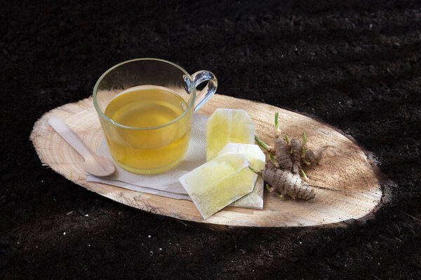 A glass with an infusion of turmeric alongside its sprouting seeds standing on a log of pine tree with a soil background - Glycyrrhiza glabra