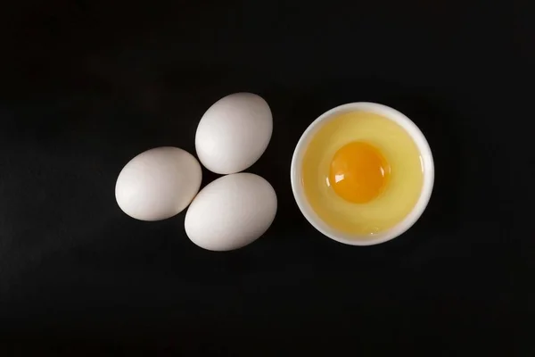 Hava manzarası: siyah arkaplanda üç beyaz yumurta, hemen yanında, yumurta sarısı ve beyaz bir tabak.