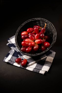 Hasır sepette bir demet üzüm, siyah arkaplanda.