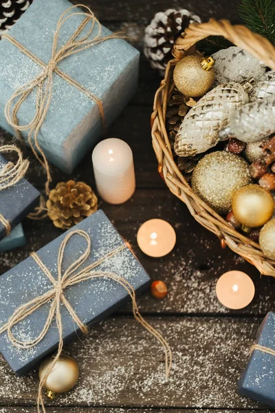 Festliche Geschenke mit Schachteln, Kerze, Schnee, Nadelholz, Korb, Zimt, Tannenzapfen, Nüssen auf Holzgrund. — Stockfoto