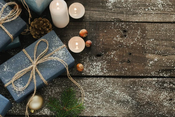 Festliche Geschenke mit Schachteln, Kerze, Schnee, Nadelholz, Korb, Zimt, Tannenzapfen, Nüssen auf Holzgrund. — Stockfoto