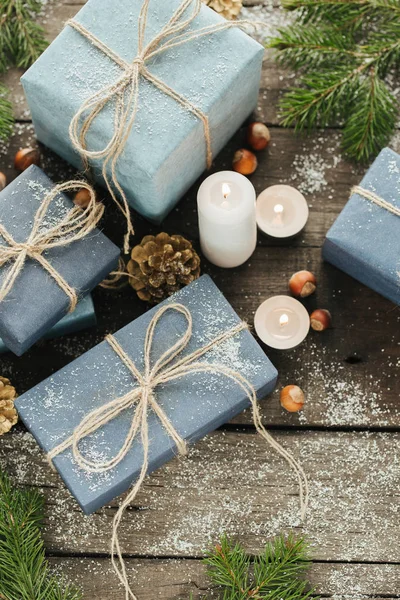 Festliche Geschenke mit Schachteln, Kerze, Schnee, Nadelholz, Korb, Zimt, Tannenzapfen, Nüssen auf Holzgrund. — Stockfoto