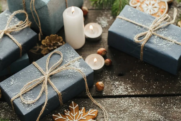 Festliche Geschenke mit Schachteln, Kerze, Schnee, Nadelholz, Korb, Zimt, Tannenzapfen, Nüssen auf Holzgrund. — Stockfoto