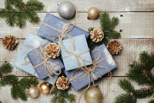 Festliche Geschenke mit Schachteln, Kerze, Schnee, Nadelholz, Korb, Zimt, Tannenzapfen, Nüssen auf Holzgrund. — Stockfoto