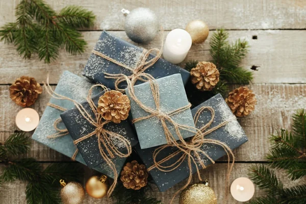 Presentes festivos com caixas, vela, neve, coníferas, cesta, canela, pinheiros, nozes em fundo de madeira . — Fotografia de Stock