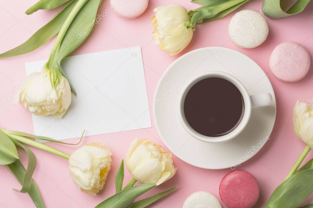 Spring morning concept. Flat-lay of cup of coffee with white flowers and macarons over light pink background, top view with space for your text