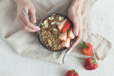 Sağlıklı kahvaltı. Granola, çilek ve kadının elinde fındık ile gri seramik kase. Diyet ve vejetaryen gıda kavramı