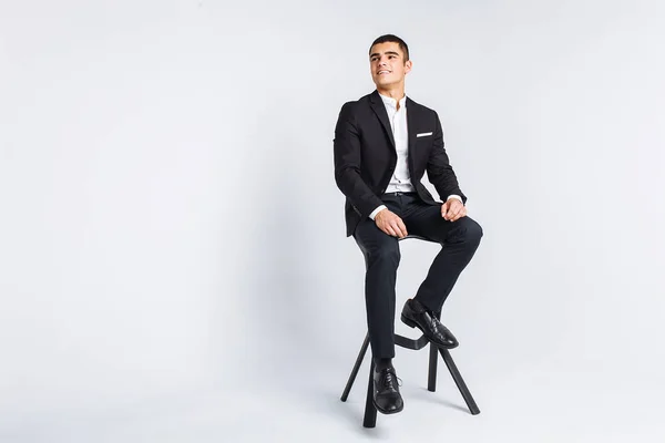 Porträt der Schönen, die in einem Studio posiert, weißer Hintergrund, stilvoller Geschäftsmann, stilvoller Mann, der auf einem Designerstuhl sitzt — Stockfoto