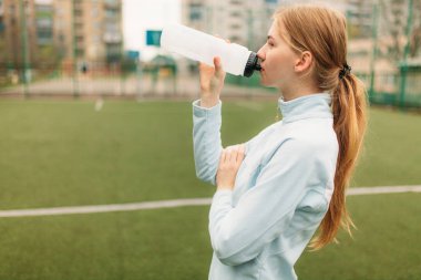 Egzersiz, içme suyu futbol sahasında kıza. Spor giyim güzel kız portresi.