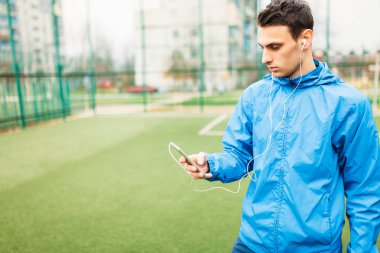 adam bir egzersiz sırasında müzik dinlemek. Genç bir adam spor çalış, futbol sahasında çalışır. Adam açık, temiz havada çalışıyor. Metin için izole yer