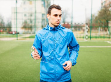 adam bir egzersiz sırasında müzik dinlemek. Genç bir adam spor çalış, futbol sahasında çalışır. Adam açık, temiz havada çalışıyor. Metin için izole yer