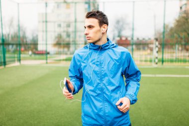 adam bir egzersiz sırasında müzik dinlemek. Genç bir adam spor çalış, futbol sahasında çalışır. Adam açık, temiz havada çalışıyor. Metin için izole yer