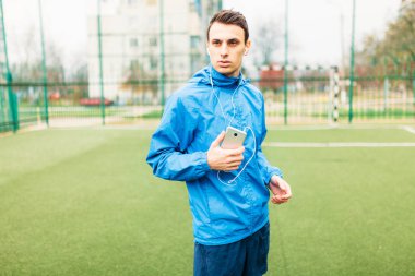 adam bir egzersiz sırasında müzik dinlemek. Genç bir adam spor çalış, futbol sahasında çalışır. Adam açık, temiz havada çalışıyor. Metin için izole yer