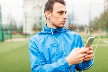 adam bir egzersiz sırasında müzik dinlemek. Genç bir adam spor çalış, futbol sahasında çalışır. Adam açık, temiz havada çalışıyor. Metin için izole yer