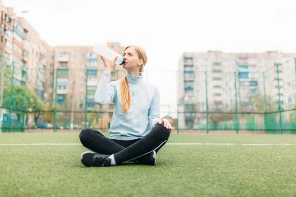 De meisje na het sporten, het drinken van water op het voetbalveld. Portret van mooi meisje in sportkleding. — Stockfoto