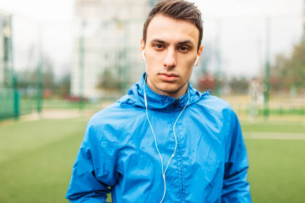 guy listen to music during a workout. A young man plays sports, runs on the football field. The guy works in the open, fresh air. Isolated place for text