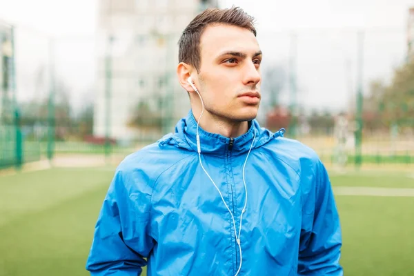guy listen to music during a workout. A young man plays sports, runs on the football field. The guy works in the open, fresh air. Isolated place for text