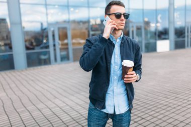 bir adam bir kağıt kahve, goes-den geçerek şehir, şık giysiler ve güneş gözlüğü, yakışıklı bir adam yapma bir telefon görüşmesi, iyi bir hava