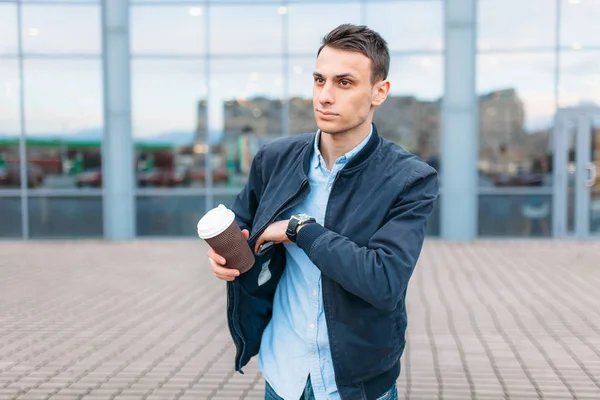 a man with a paper Cup of coffee, goes through the city, a handsome guy in stylish clothes, pulls out his phone from his pocket
