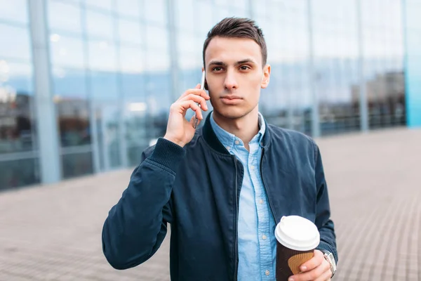 a man with a paper Cup of coffee, goes through the city, a handsome guy in stylish clothes, on the phone, good weather