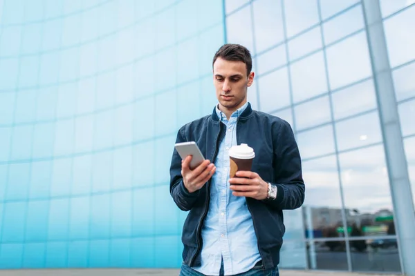 a man with a paper Cup of coffee, goes through the city, a handsome guy in stylish clothes, with phone in hand, Sunny weather