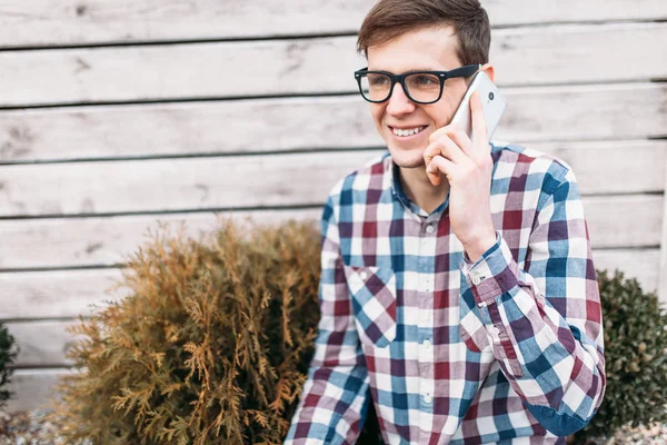 Man talking on the phone, on the background of a wooden wall, smiling, glasses and a shirt — Stock Photo, Image