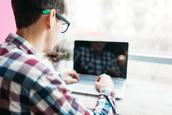 Un giovane uomo si siede in un caffè con un computer portatile, cerca in Internet, digitando sul computer portatile — Foto Stock