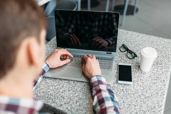 Um homem senta-se em um café e trabalhando em laptop, à procura de trabalho, o estudante escreve o dever de casa, um cara de camisa e óculos — Fotografia de Stock