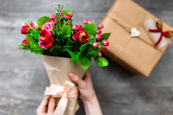 Mano femenina sosteniendo un regalo envuelto, Día de San Valentín, foto romántica. Fondo de madera gris romántico con corazones y regalos, adecuado para la publicidad — Foto de Stock