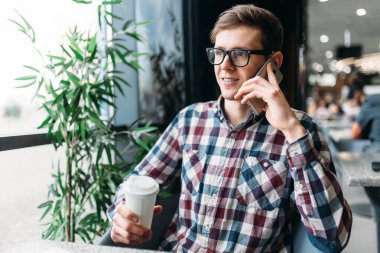 Genç adam, bir kağıt bardak tutan Evet el, bir cep telefonu ile