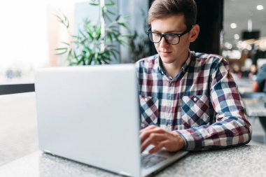 Bir adam bir kafede oturuyor ve dizüstü bilgisayar, iş, aramaya çalışan öğrenci ödev, bir adam bir gömlek ve gözlük yazıyor