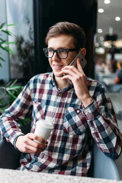 Young man with mobile phone in hand, talking on the phone, holding a paper Cup